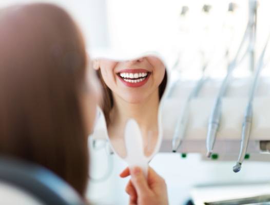 Woman looking at smile in mirror after cosmetic dentsitry