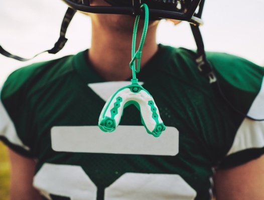 Green sportsguard hanging from football helmet